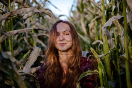 Photo for Brown-haired woman enjoys walking among corn stalks and uniting with nature. Lady walks and explores countryside nature on corn plantation - Royalty Free Image