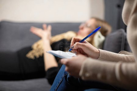 Photo for Female cient lying on couch shares childhood traumas with psychologist. Expert simultaneously records important details from patient life - Royalty Free Image