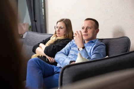 Téléchargez les photos : Psychologue écoute l'homme parler de problèmes dans la relation avec la femme. Homme assis sur un canapé gris au bureau - en image libre de droit