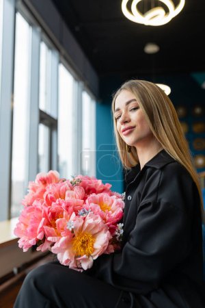 Photo for Young businesswoman receives bouquet of flowers from team members on birthday. Contented female employee holds flower arrangement in lounge area - Royalty Free Image