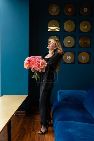 Foto de Mujer despreocupada se levanta y sostiene ramo de flores en la zona de salón del personal. Empleada disfruta de olor fragante de arreglo de flores en la habitación - Imagen libre de derechos