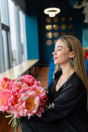 Téléchargez les photos : Femme d'affaires se détend avec une agréable odeur de bouquet dans le salon du personnel. Une employée ferme les yeux pour profiter du parfum des fleurs - en image libre de droit