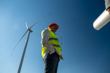 Photo for Windmill blades rotate under blue sky. Professional technician meets with general manager of project under wind generator side low angle shot - Royalty Free Image