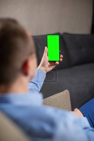 Photo for Busy male psychologist sits in armchair and looks at screen of mobile phone. Man mobile phone has chromakey for inserting photo or video - Royalty Free Image