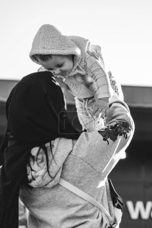 Téléchargez les photos : KYIV, UKRAINE - 27 SEPTEMBRE 2021 : Adorable tout-petit garçon sourit et rit lancé par les bras de la mère. Le parent portant le hijab noir soulève l'enfant vers le ciel et fait preuve d'amour. Plan noir-blanc - en image libre de droit