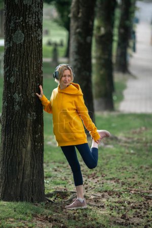 Photo for A woman wearing headphones warms up in the park before jogging. - Royalty Free Image