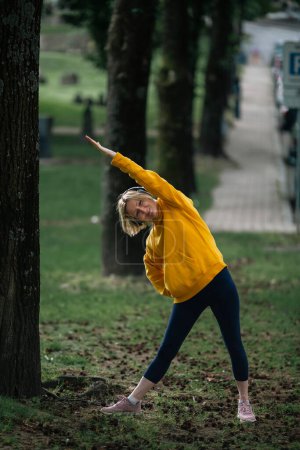 Photo for A woman wearing headphones exercises in the park. - Royalty Free Image