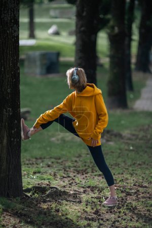 Photo for A woman wearing headphones warms-up up in the park. - Royalty Free Image