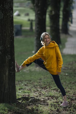 Photo for A woman wearing headphones warms up in the park before jogging in the Park. - Royalty Free Image