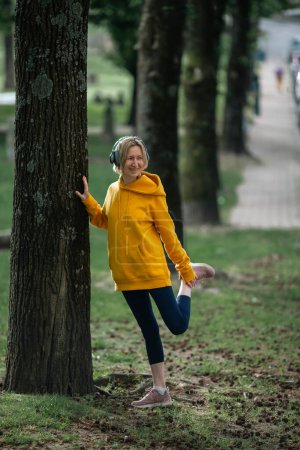 Photo for A woman wearing headphones doing exercises outdoor in the Park. - Royalty Free Image