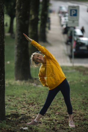 Photo for A woman wearing headphones doing exercises outdoor. - Royalty Free Image