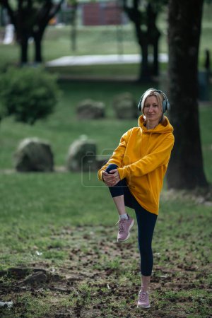 Photo for A woman wearing headphones exercises outdoor in the Park. - Royalty Free Image