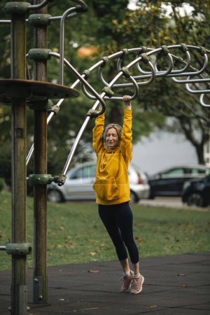 Photo for A woman wearing headphones exercising outdoors in an outdoor playground. - Royalty Free Image