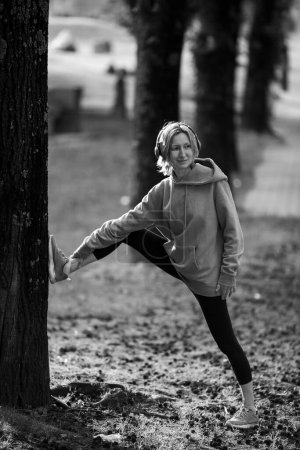 Photo for A woman wearing headphones doing exercises outdoor in the Park. Black and white photo. - Royalty Free Image