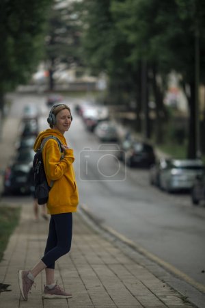 Photo for A woman wearing headphones walks down the sidewalk after a workout. - Royalty Free Image