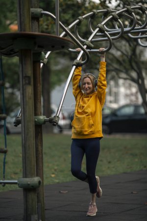 Photo for A woman wearing headphones on gym equipment in the park. - Royalty Free Image