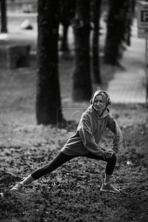 Photo for A woman wearing headphones is exercising outdoors. Black and white photo. - Royalty Free Image