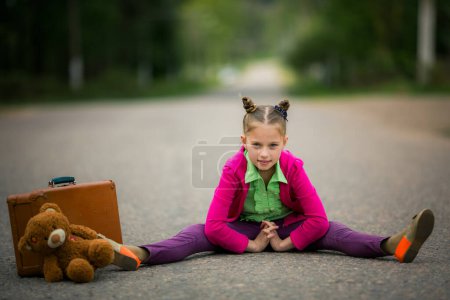Helle Reise. Ein junges Mädchen in lebendiger Kleidung steht mit einem Koffer und einem Stofftier auf der Straße, bereit für ein Abenteuer.