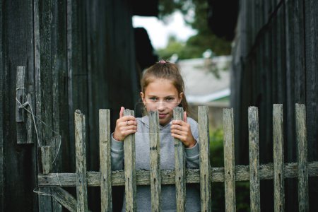 Una adolescente junto a una valla de madera, su rostro expresando tranquila determinación y ternura.