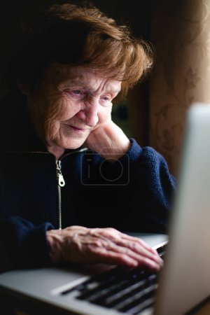Eine ältere Frau sitzt mit ihrem Laptop, gebadet in ihrem weichen Schein, ihr Gesicht ruhig, vertieft in digitale Verfolgungsjagden.