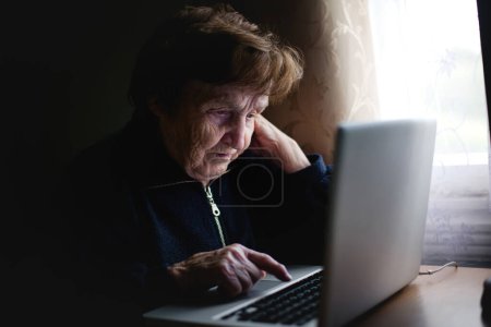 In einer gemütlichen Szene benutzt eine ältere Dame bequem ihren Laptop und fügt moderne Technik nahtlos in ihre Routine ein.