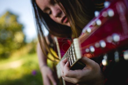 Una chica inmersa en tocar la guitarra, destacando los intrincados detalles de sus dedos en las cuerdas, con la cara suavemente borrosa en el fondo.