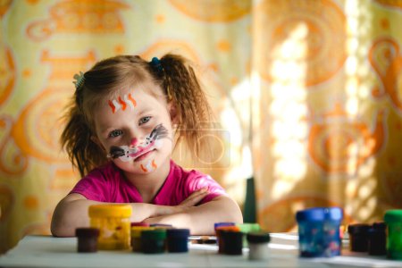 A young girl with a painted face enjoys the creative process of painting, her expression filled with joy and concentration.