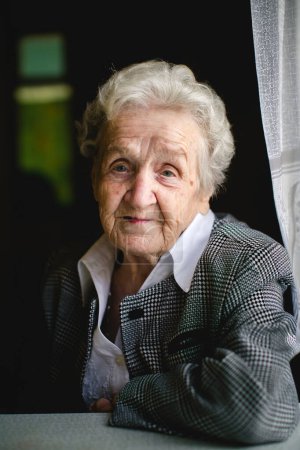 Une dame âgée s'assied à une table, capturée dans un portrait réfléchi qui reflète sa sagesse et sa grâce.