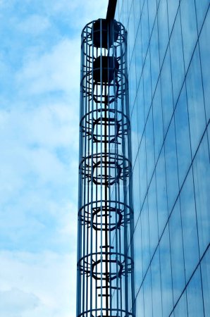 Foto de Pared de cristal y escalera de caracol en edificio de oficinas moderno con fondo de cielo azul - Imagen libre de derechos