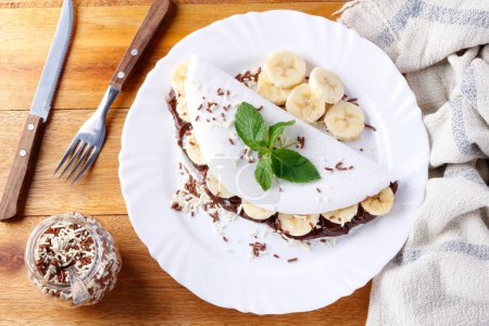 Foto de Tapioca casera o beiju rellenos de plátano y chocolate en plato blanco sobre mesa de madera rústica. vista superior - Imagen libre de derechos