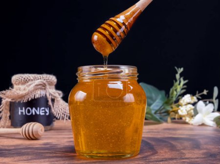 Honiglöffel, der in Zeitlupe aus dem mit Honig gefüllten Glas kommt. Honig enthält viele Nährstoffe, Antioxidantien, verbessert die Herzgesundheit, die Wundversorgung, bietet antidepressive und angstlösende Wirkung