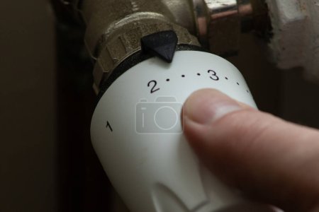 Téléchargez les photos : Close up hand adjusting heating temperature. Reducing heating cost in crisis. War in Ukraine. Energy crisis. regulating temperature knob - en image libre de droit