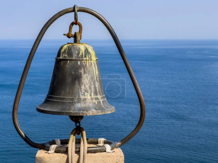 Capture the essence of seafaring history with this stunning image featuring an aged bronze bell against a tranquil ocean backdrop. The bells weathered surface and dark metal frame tell a tale of maritime tradition.