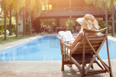 Photo for Relaxation concept, woman reading book near swimming pool of hotel - Royalty Free Image