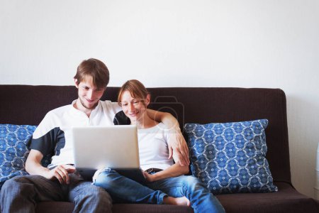 Foto de Joven pareja mirando a la computadora y sonriendo, familia sentada en el sofá en casa - Imagen libre de derechos