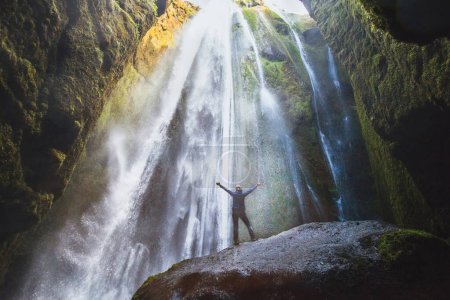 Travel to Iceland, person with raised hands standing in waterfall Gljufrabui, inspired happy traveler enjoying nature, adventure concep