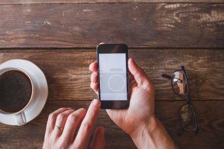 Hand hält Smartphone mit leerem Bildschirm auf Holzgrund