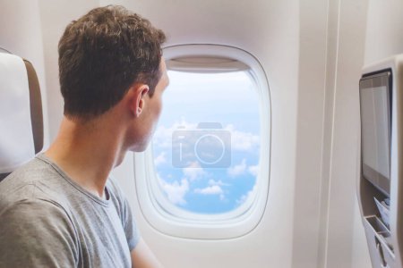 Téléchargez les photos : Voyageur regardant la fenêtre dans l'avion, voyage en avion, touriste homme assis dans l'avion - en image libre de droit