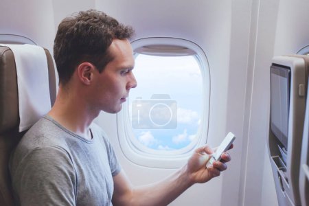 Foto de Pasajero usando teléfono móvil smartphone en el avión, conexión wifi en el avión durante el vuelo - Imagen libre de derechos