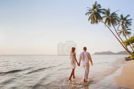 Téléchargez les photos : Romantique jeune couple marchant ensemble sur belle plage tropicale exotique au coucher du soleil - en image libre de droit