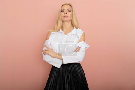 Beauté, portrait de mode. Style d'affaires élégant. Portrait d'une belle femme blonde en chemisier blanc et jupe noire posant en studio sur un fond rose.