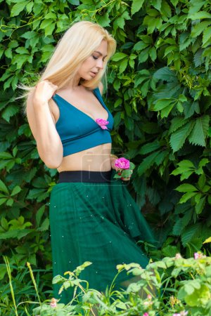 Foto de Hermosa modelo rubia de moda disfrutando de la naturaleza, respirando aire fresco en el jardín de verano sobre el fondo de hojas verdes. Concepto de armonía - Imagen libre de derechos