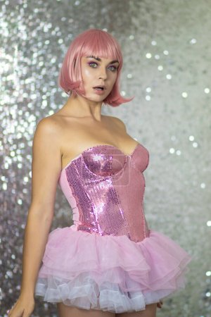 Foto de Mujer con peluca rosa y pelo corto sobre fondo plateado brillante. Vestido rosa brillante. Princesa, bailarina. Concepto de Halloween. Enfoque suave - Imagen libre de derechos