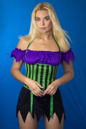 Foto de Joven mujer rubia hermosa en un disfraz de bruja sobre un fondo azul. Vestido corto, pelo largo. Concepto de Halloween. Enfoque suave - Imagen libre de derechos