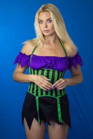 Photo for Young beautiful blonde woman in a witch costume on a blue background. Short dress, long hair. Halloween concept. Soft focus - Royalty Free Image