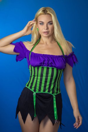 Téléchargez les photos : Jeune belle femme blonde en costume de sorcière sur fond bleu. Robe courte, cheveux longs. Concept d'Halloween. Concentration douce - en image libre de droit
