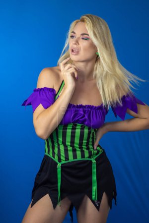Foto de Joven mujer rubia hermosa en un disfraz de bruja sobre un fondo azul. Vestido corto, pelo largo. Concepto de Halloween. Enfoque suave - Imagen libre de derechos