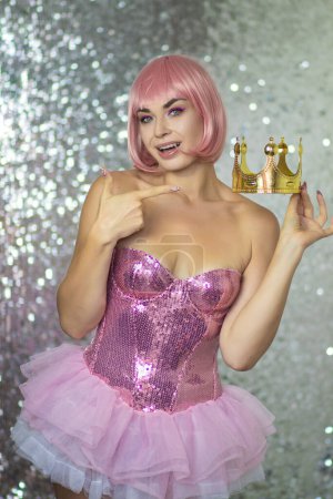 Photo for Woman in a pink wig and a bright shiny princess dress on a silver background in the studio. She wears a crown on her head. Soft focus. Halloween - Royalty Free Image