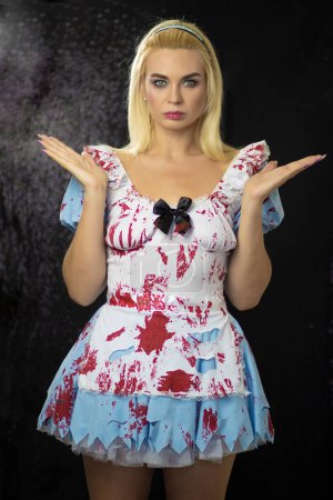 Photo for Beautiful young blonde woman in an Alice costume. The dress is torn and stained with fake blood. Halloween concept. Soft focus - Royalty Free Image
