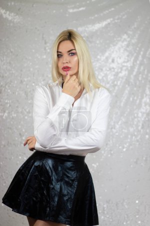Foto de Modelo rubia de moda mujer en camisa blanca y falda negra con pajarita, en el estilo del surrealismo pop gótico, fondo gris claro y blanco, xmaspunk, plata y negro, arrugado - Imagen libre de derechos